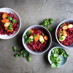 three white bowls filled with food on top of a cement floor next to green leaves