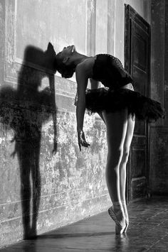 black and white photograph of a ballerina leaning against a wall with her shadow on the wall