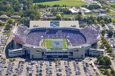 an aerial view of a football stadium with cars parked in the parking lot and lots of trees