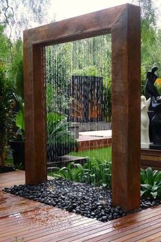 an outdoor fountain in the middle of a wooden deck with rocks and plants surrounding it