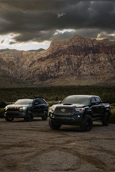 three trucks parked in front of mountains under a cloudy sky