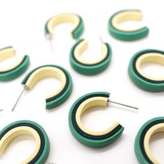 several pairs of green and yellow earrings on a white surface with pins in the middle