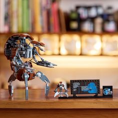 a lego robot sitting on top of a wooden table next to a book shelf filled with books