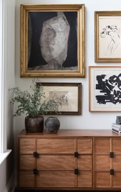 a room with pictures, paintings and vases on the wall next to a dresser