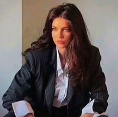 a woman sitting at a desk in front of a laptop computer wearing a suit and tie