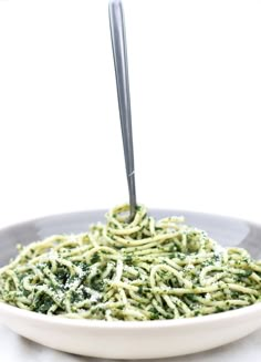 a white bowl filled with green pasta and pesto sauce on top of a table