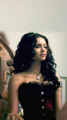 a woman in a black corset is standing near a mirror and looking into the distance