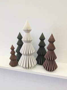 three folded paper christmas trees sitting on top of a white shelf next to each other