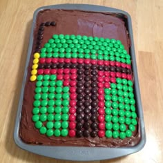 a chocolate cake with green, red and yellow decorations on it sitting on a wooden table