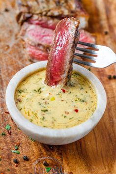 a piece of meat is being dipped into a bowl of soup with a fork in it