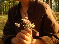 a woman sitting on the ground holding a flower in her hand and looking at it