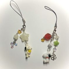 two pairs of earrings with charms attached to them on a white surface, one has a dog and the other is a cat