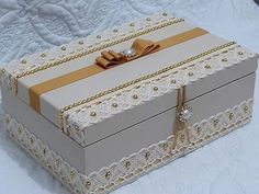 a white box with gold trimmings and bows on the lid sitting on a bed