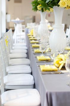 a long table with white chairs and yellow flowers in vases on each one side