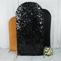 a black and gold sequined chair next to a white wall with flowers on it