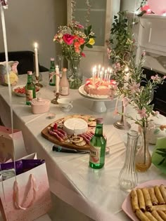 a table topped with lots of food and candles next to bottles of wine on top of a white table cloth