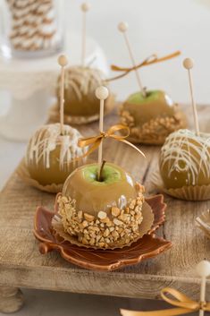 caramel apples with sprinkles and nuts are on a wooden platter