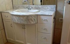 a white bathroom sink sitting under a mirror next to a cabinet with drawers and cupboards