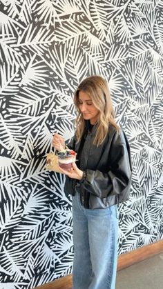 a woman standing in front of a wall holding a piece of cake and looking at it