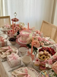 a table is set with pink and white desserts, pastries, and candles