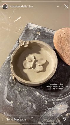 a clay bowl sitting on top of a table next to a heart shaped rock in the sand