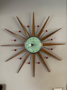 a clock mounted to the side of a wall with wooden sticks and red dots on it