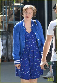 a woman in a blue dress and jacket walking down the street with a man behind her