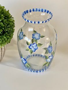 a glass vase with blue flowers painted on it next to a potted green plant