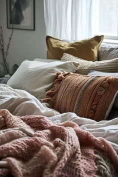 an unmade bed with pillows and blankets on it, in front of a window