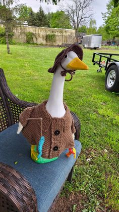 a duck wearing a sweater and hat sitting on a bench in the grass next to a trailer