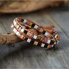 two leather bracelets sitting on top of a piece of wood next to a tree branch