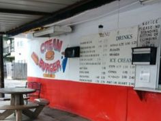 an empty table and bench in front of a food stand with menus on the wall