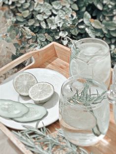 a wooden tray topped with glasses filled with water and sliced lemons on top of a white plate