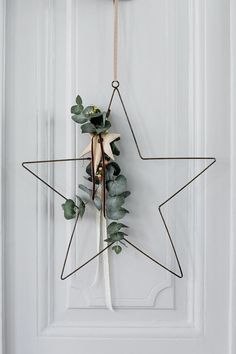 a star decoration hanging on a door with eucalyptus leaves and other greenery attached to it