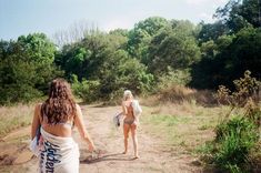 two women in bathing suits walking down a dirt road