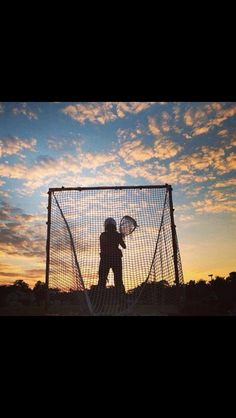 a person standing in front of a soccer goal with the sun setting behind them and clouds