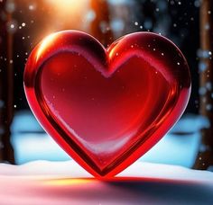 a red glass heart sitting on top of snow covered ground in the middle of winter