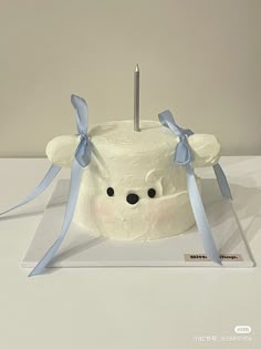 a white cake with blue ribbon around it and a candle in the shape of a bear