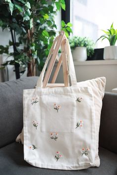 a white tote bag sitting on top of a couch next to a potted plant