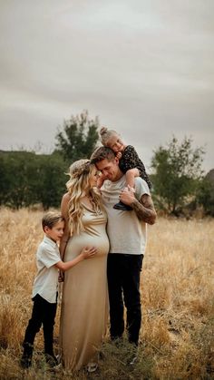 a pregnant woman and two young boys are standing in a field with their arms around each other