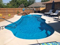 an empty swimming pool with lounge chairs and umbrellas in the back yard next to it