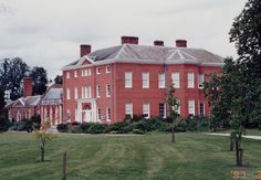 a large red brick building sitting in the middle of a lush green field next to trees