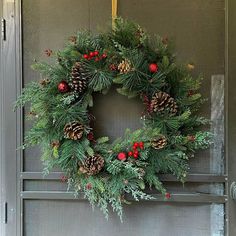 a wreath hanging on the front door of a house with pine cones and red berries