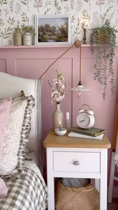 a bedroom with pink walls and flowers on the bedside table next to it is an alarm clock