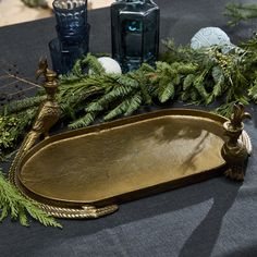 a gold tray with pine branches and candles on the side, surrounded by evergreen leaves