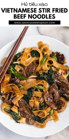 a white plate topped with beef and noodles next to chopsticks on a table