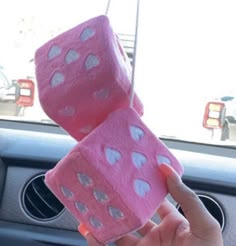 someone is holding two pink dices in their hand while they are sitting in the car