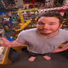 a man sitting at a table with his hands in the air, surrounded by legos