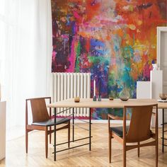 a dining room table with two chairs and a large painting on the wall behind it