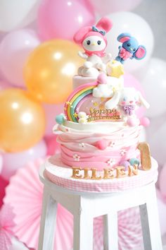 a hello kitty birthday cake sitting on top of a table with balloons in the background